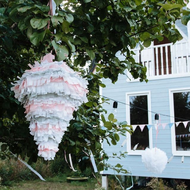 A handmade pastel piñata hanging in a garden apple tree