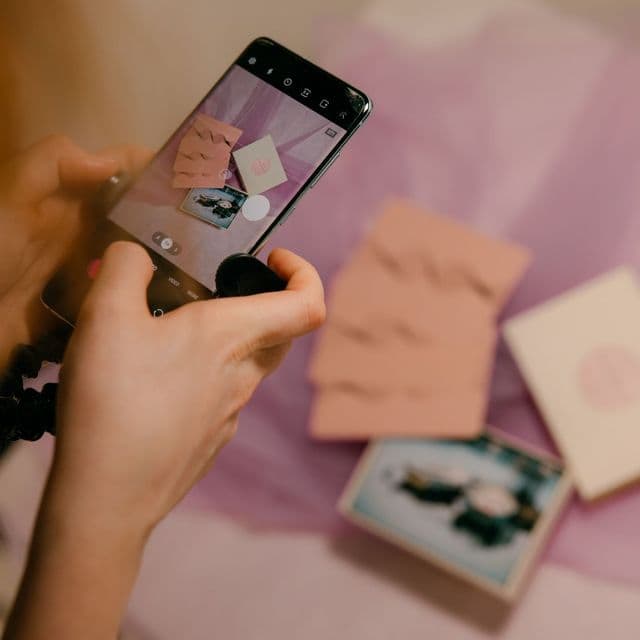 Hands photographing a pink invitation suite with a phone