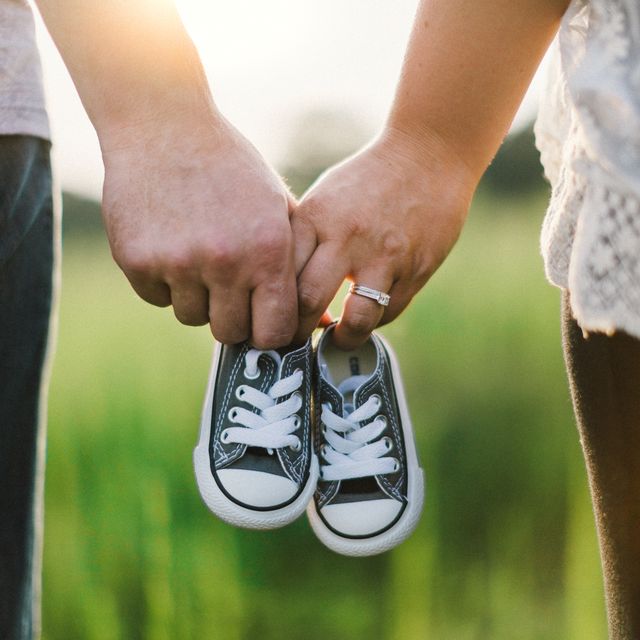 A hand holding a tiny baby sneaker over sunlit grass