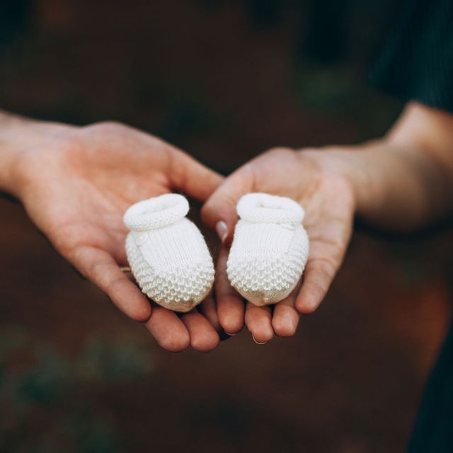 Two hands holding a pair of tiny white baby booties